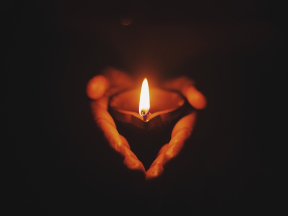 two hands holding a candle in the dark