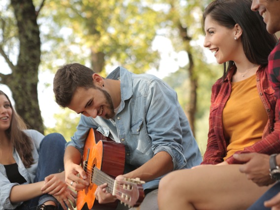 group of people sitting outdoors and playing the guitar
