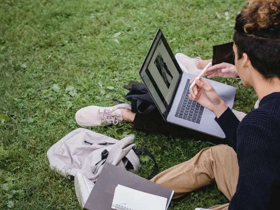 two students sitting in the grass and looking at a laptop computer together