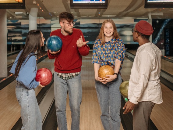 group of friends standing in front of a bowling lane holding bowling balls