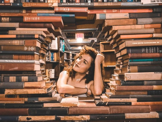 a person's face visible behind a large stack of books