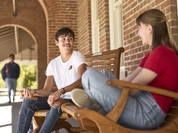 two people sitting on wood benches in front of a brick building