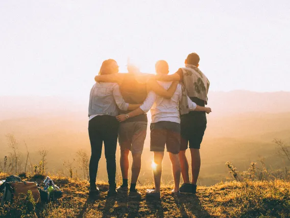 Group of 4 friends with arms over one another outside