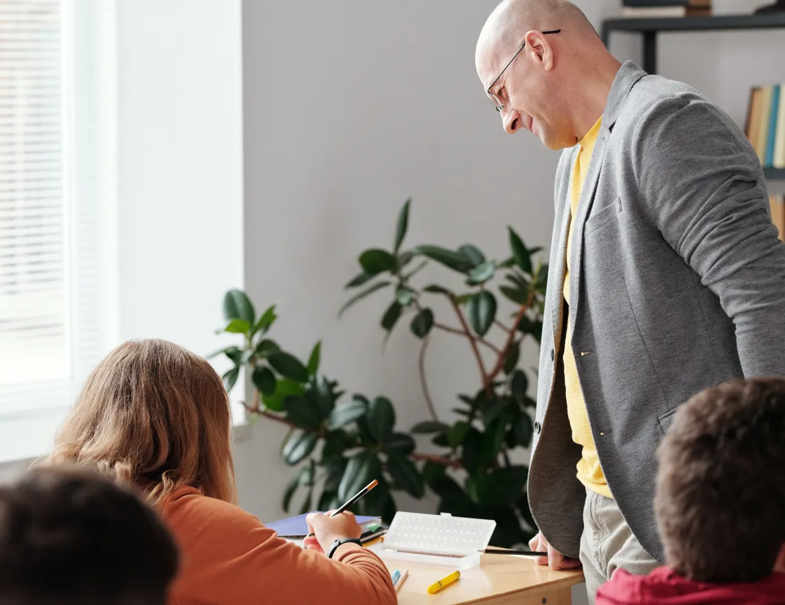 teacher standing next to a student sitting in a desk