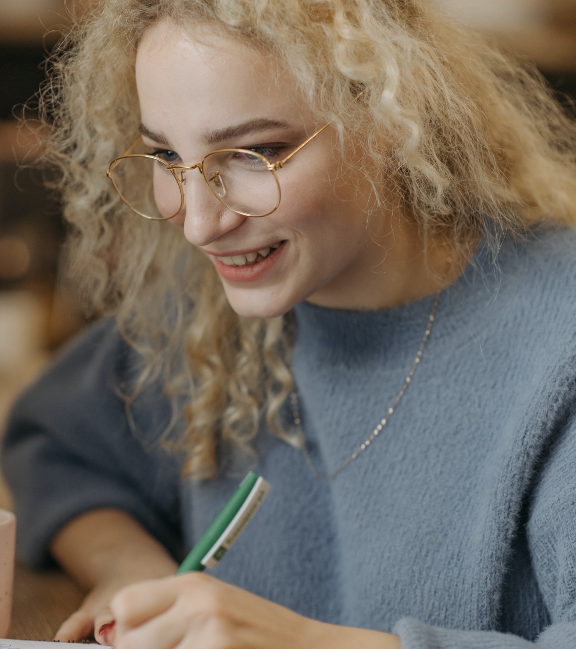 person wearing glasses smiling and writing in a notebook
