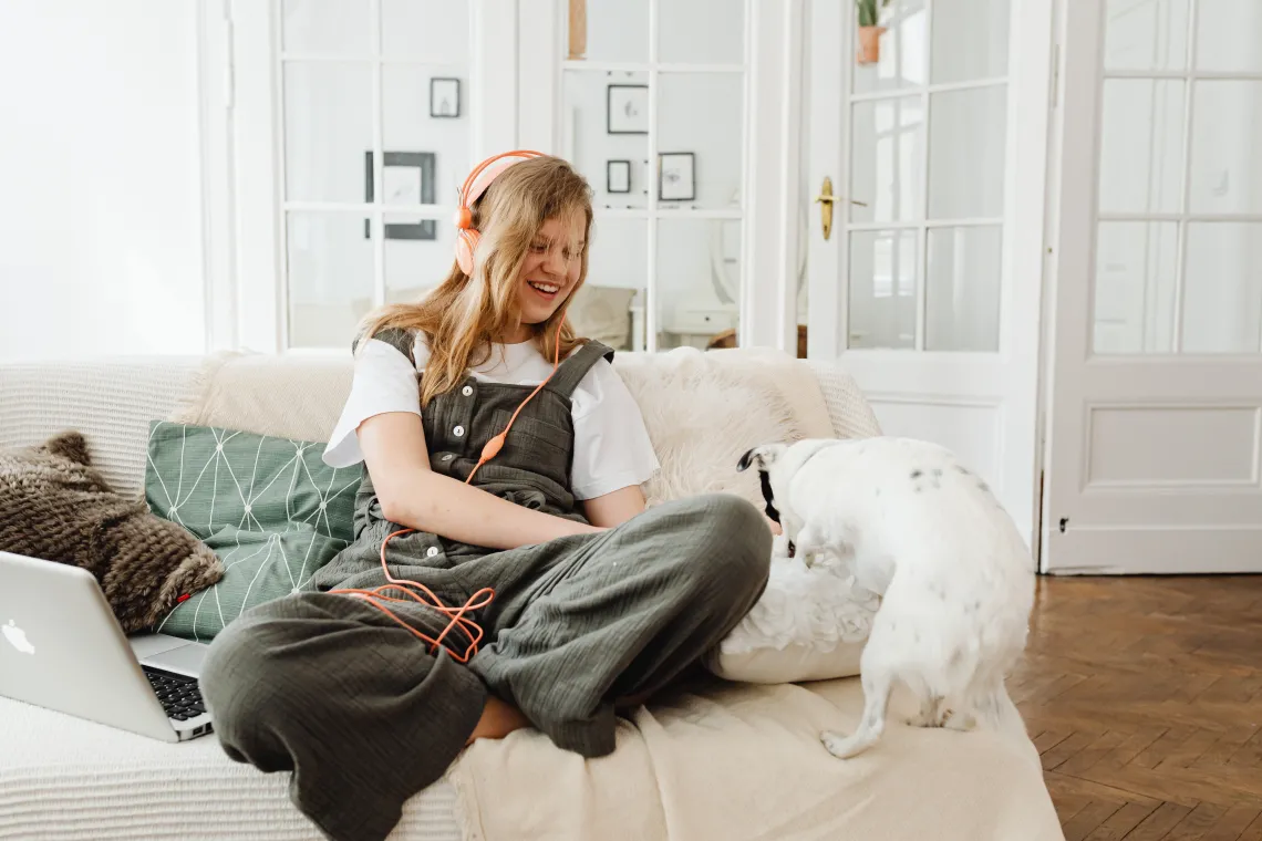 person sitting on a couch wearing headphones and petting a dog