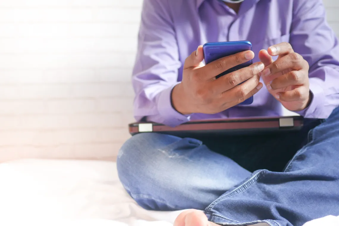 person sitting on a bed holding a smart phone in their hands