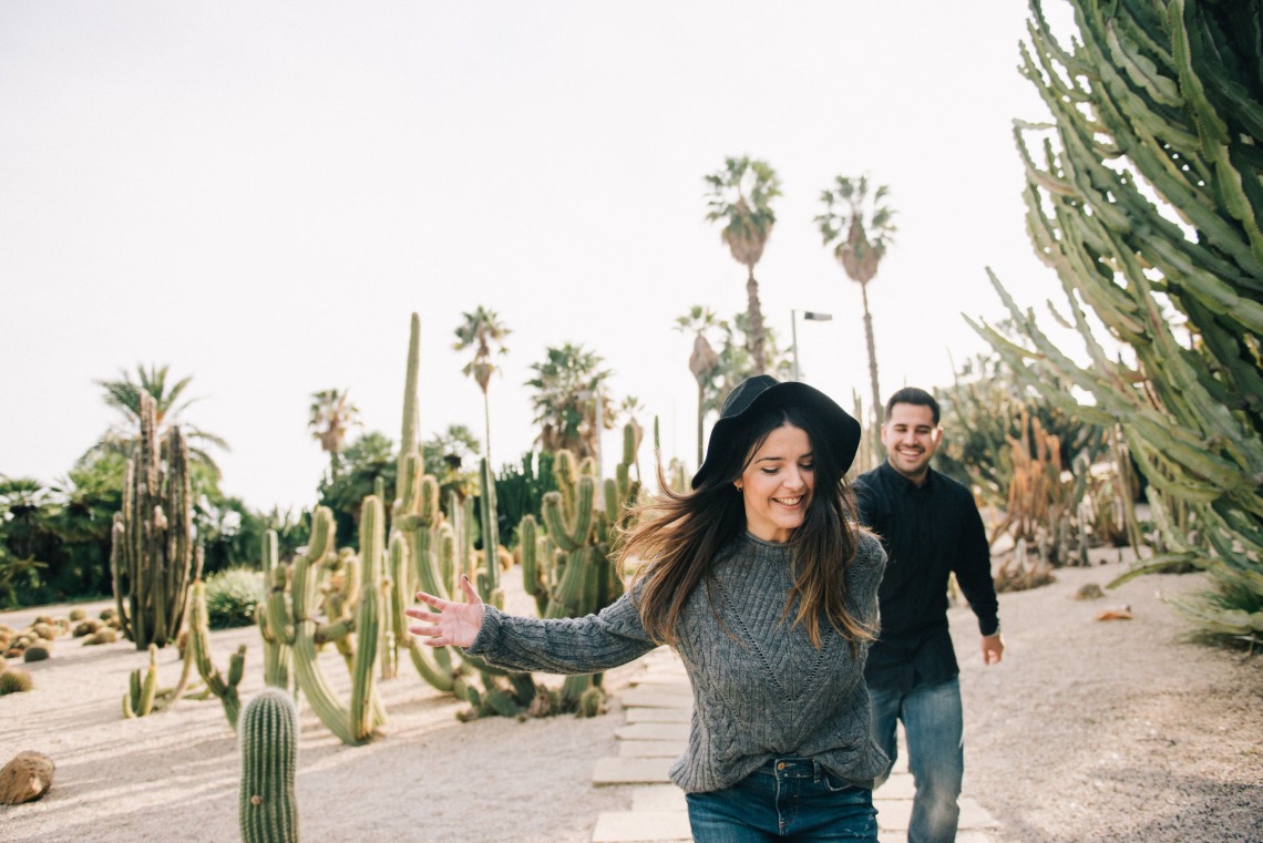 two people walking in the desert with cacti and palm trees in the background