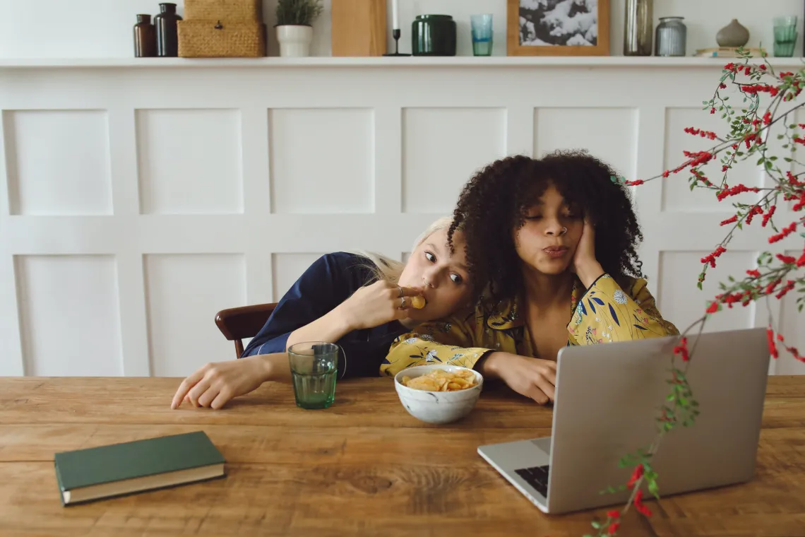 two people eating a snack and watching someone on a laptop