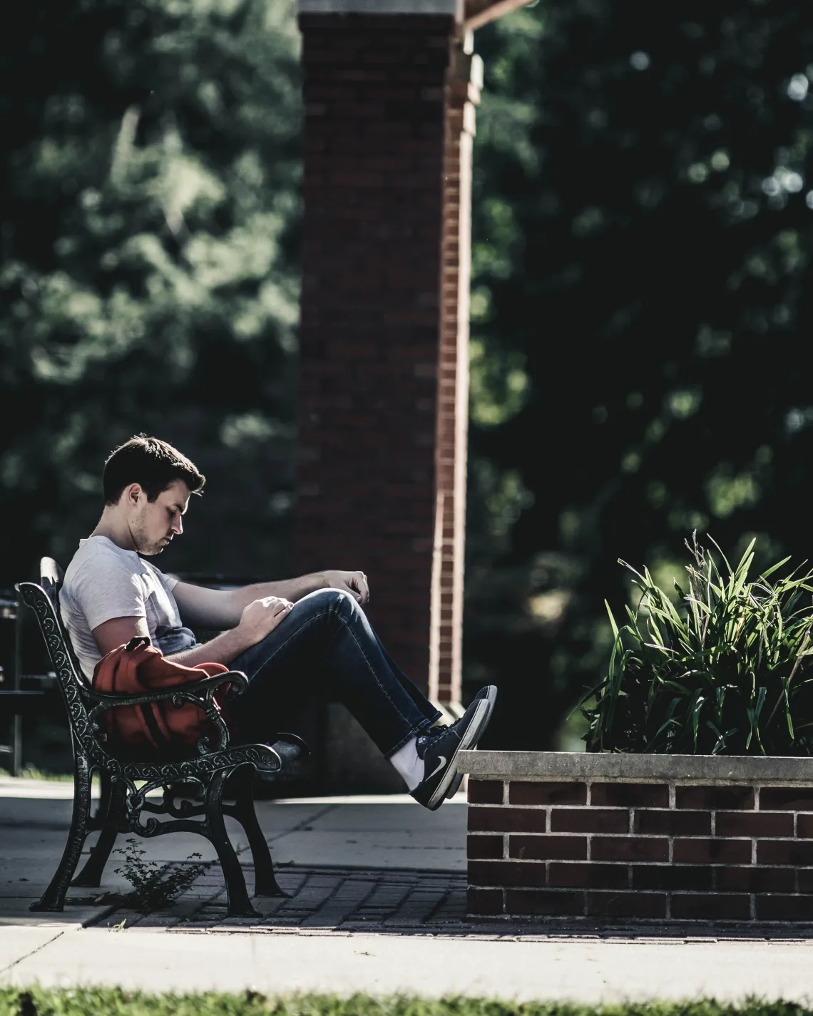 person sitting on a bench resting their feet on a short brick wall