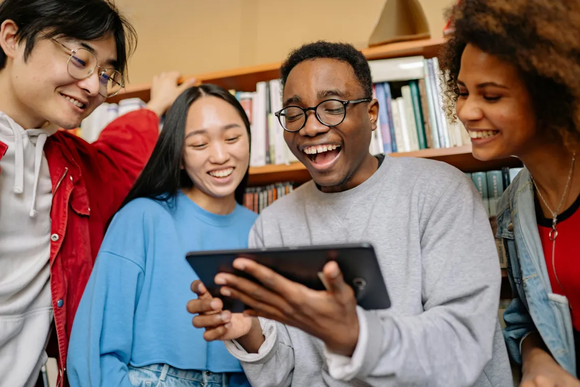 group of people looking at a tablet with a library book shelf visible in the background