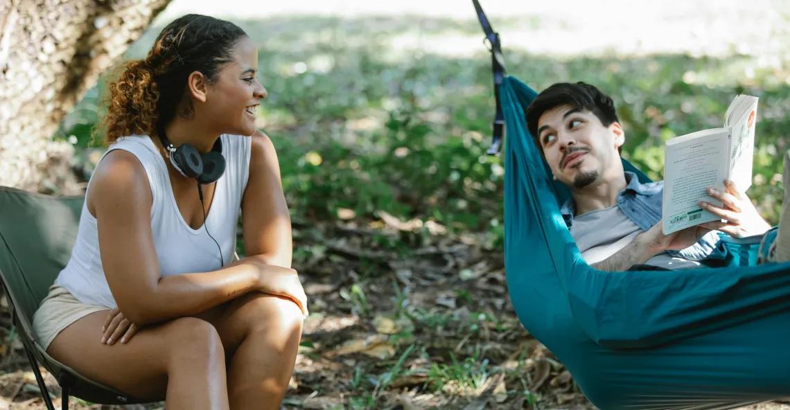 a person sitting in a chair beside another person sitting in a hammock outdoors