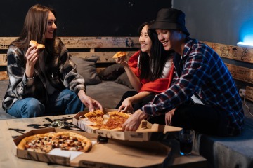 group of people sitting on a bench and eating pizza