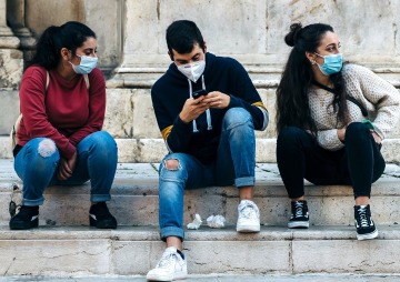 three people wearing surgical masks sitting on the steps to a building